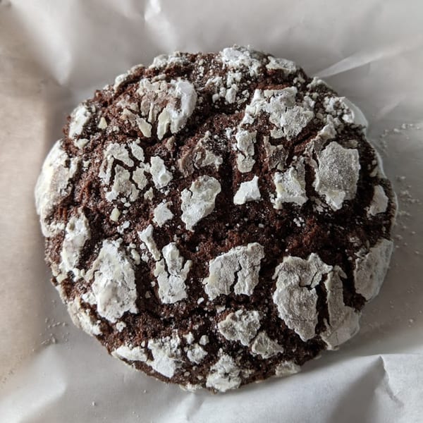 A close-up of a Sweetspot chocolate crinkle cookie, dusted with powdered sugar, on white parchment paper.