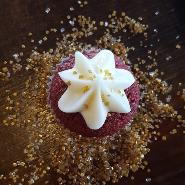 Red velvet cupcake with white frosting and gold sprinkles on a wooden surface.
