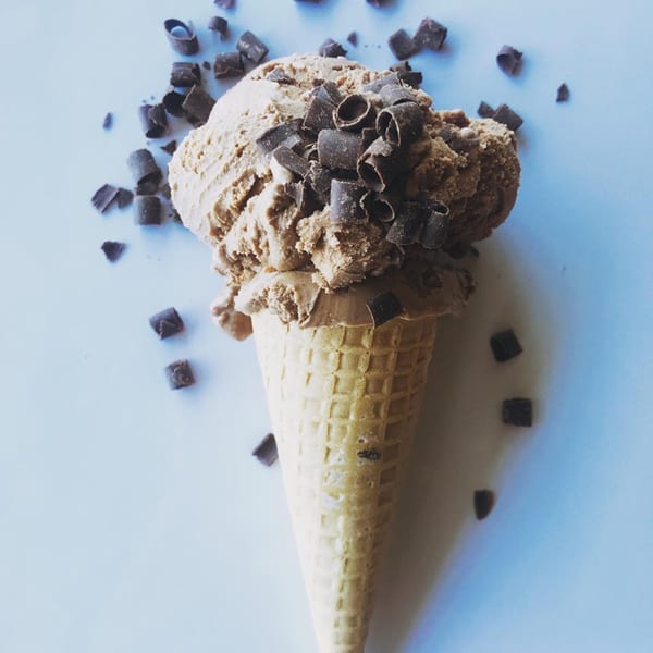 Sweetspot's chocolate ice cream in a waffle cone, topped with chocolate shavings, on a light blue surface.